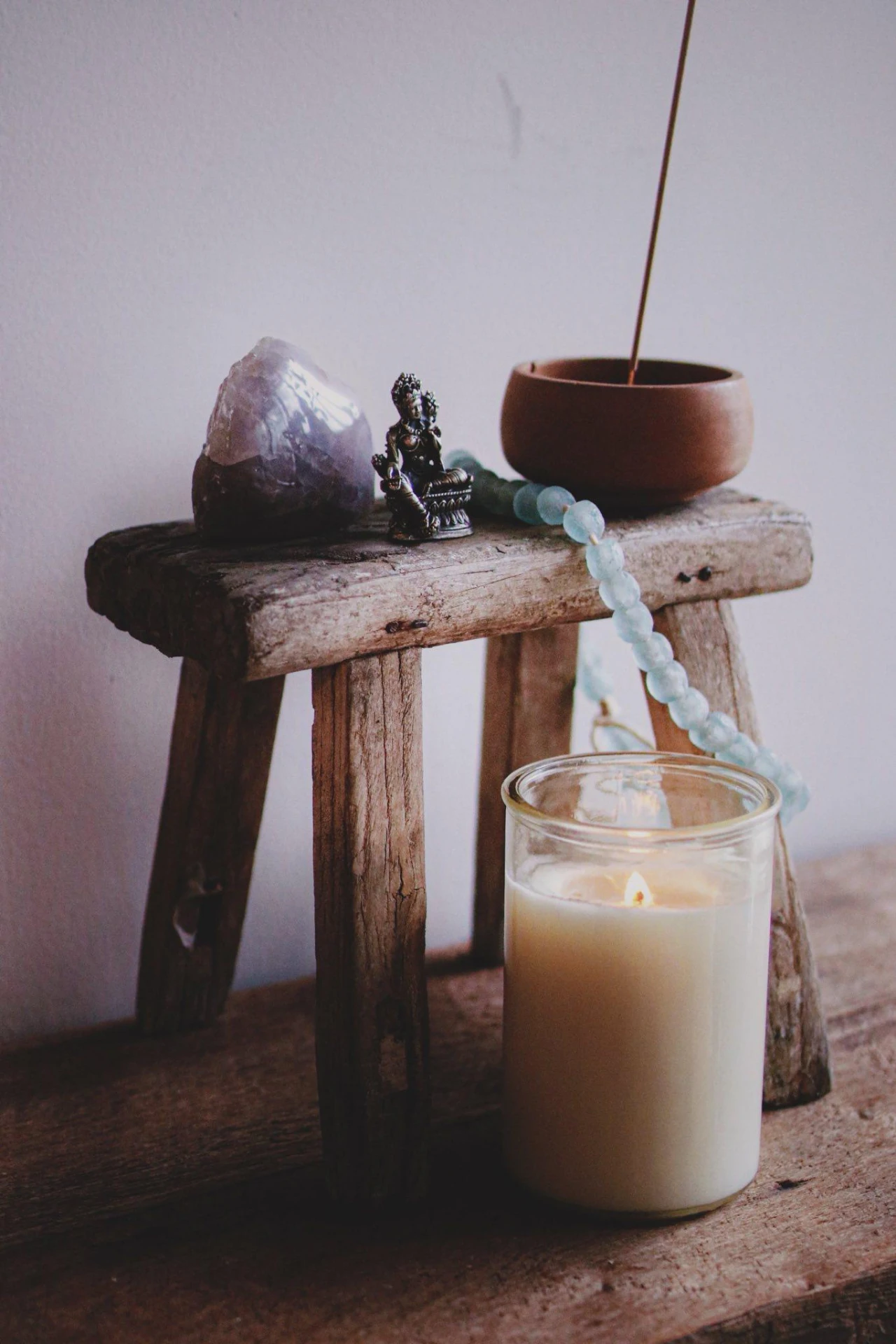 A candle, crystal, statue, beads and incense arranged on a wooden stool